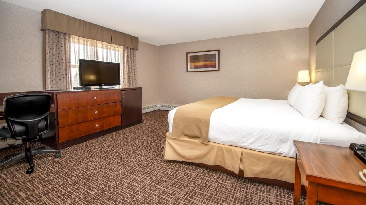 A hotel room with a bed, desk, chair, TV, and wooden furniture.