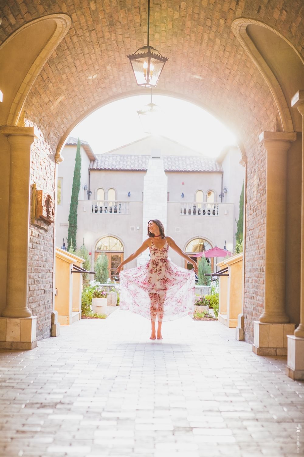 Woman standing under the courtyard archways with arms spread wid