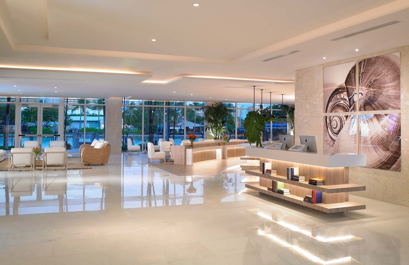 A wide view of a modern hotel lobby with a reception desk, seating area, and large windows.