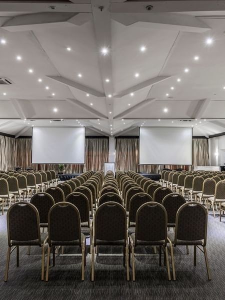 Vusu Boardroom with rows of chairs by two large screens under a white vaulted ceiling at Warwick Fiji Resort and Spa