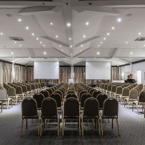 Vusu Boardroom with rows of chairs by two large screens under a white vaulted ceiling at Warwick Fiji Resort and Spa