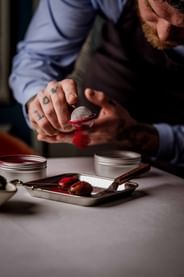 Chef Tom Brown dusting red powder through a sieve onto small bites on a tray in Tom Brown at The Capita
