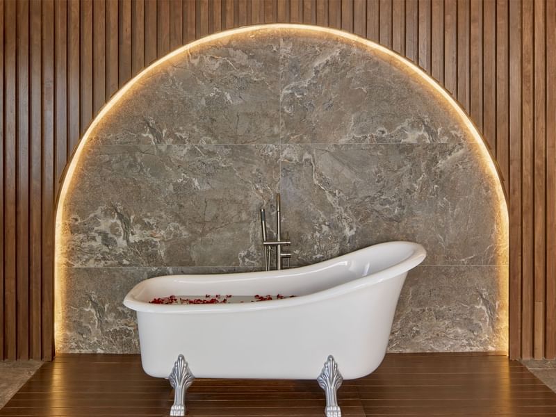 Luxurious freestanding bathtub with rose petals, set against a stylish marble wall at Fiesta Americana