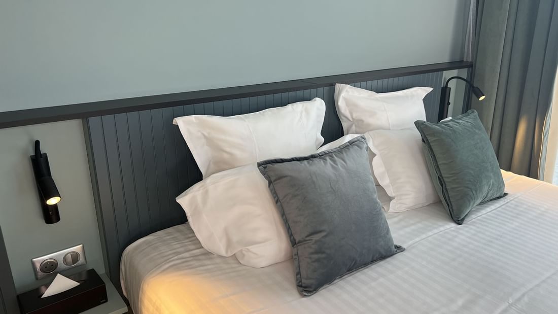 Lit avec plusieurs oreillers, éclairage mural, et boîte de mouchoirs sur une table de chevet.