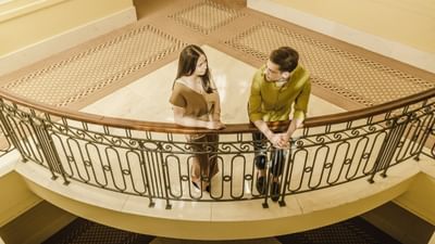 Couple conversing on an ornate circular balcony overlooking an interior space at Polonia Palace Hotel