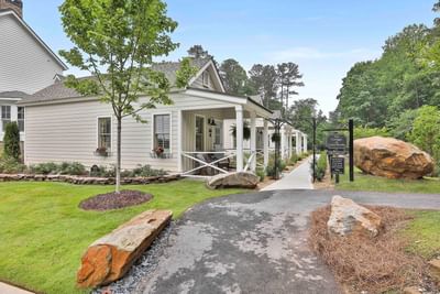 Charming cottages surrounded by lush greenery, with a pathway leading to The Cottages at Laurel Brooke entrance