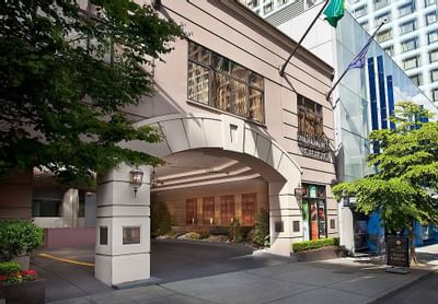 The main entrance of The Paramount Hotel Seattle on a sunny day with trees and a valet parking sign