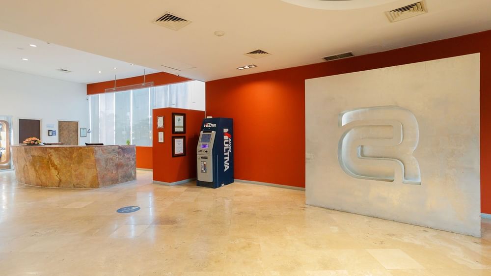Bright lobby featuring a stone reception desk, red walls, and a large wall logo at Camino Real Pachuca