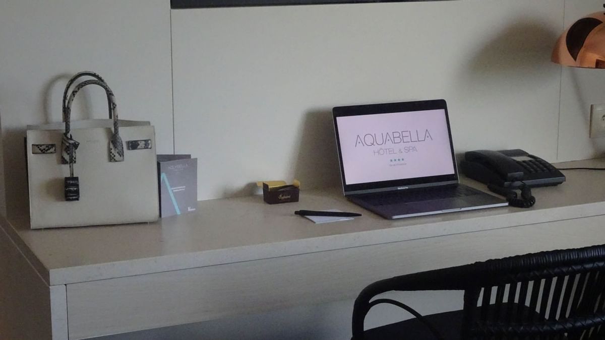 Bureau avec ordinateur portable ouvert, sac à main, téléphone, stylo, boîte, et chaise.