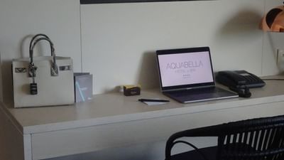 Bureau avec ordinateur portable ouvert, sac à main, téléphone, stylo, boîte, et chaise.