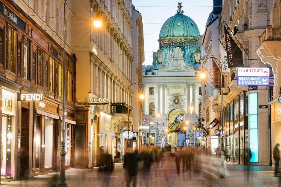 Kohlmarkt in Vienna at dusk with illuminated luxury shops, blurred pedestrians and view of the Hofburg