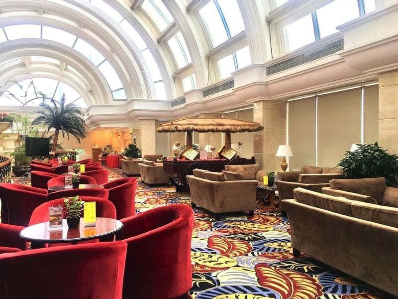 Oasis Lounge featuring red velvet armchairs under arched glass windows at Celebrity International Grand Hotel