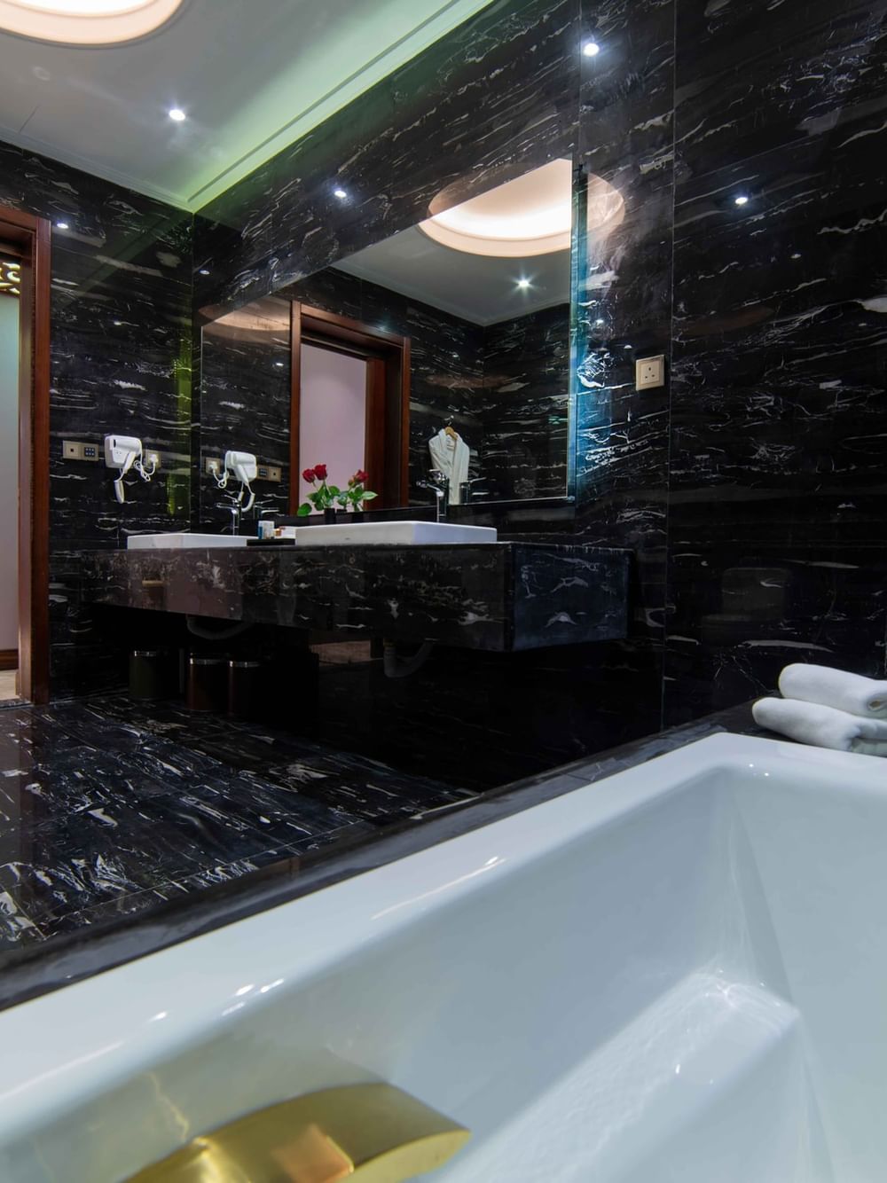 White soaking tub by black marble walls & a large vanity mirror in Penthouse Villa entrance at Warwick Al Khobar