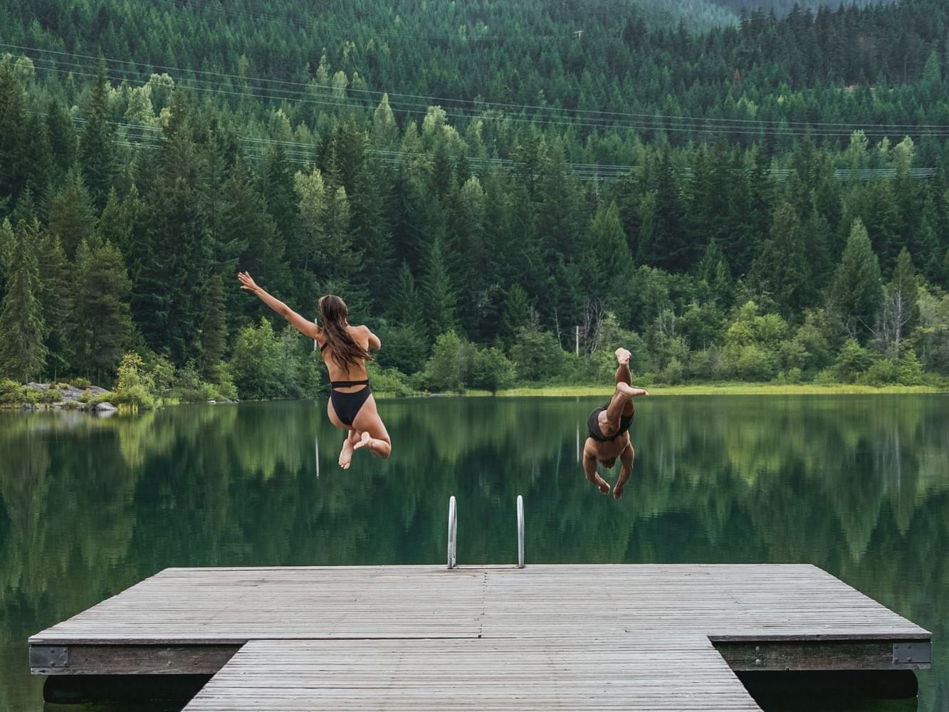 Couple diving into a lake with a mountain view, Nita Lake Lodge