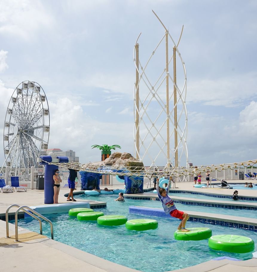 Child playing in the water park at Margaritaville Resort Biloxi, with a Ferris wheel and rope bridge in the background