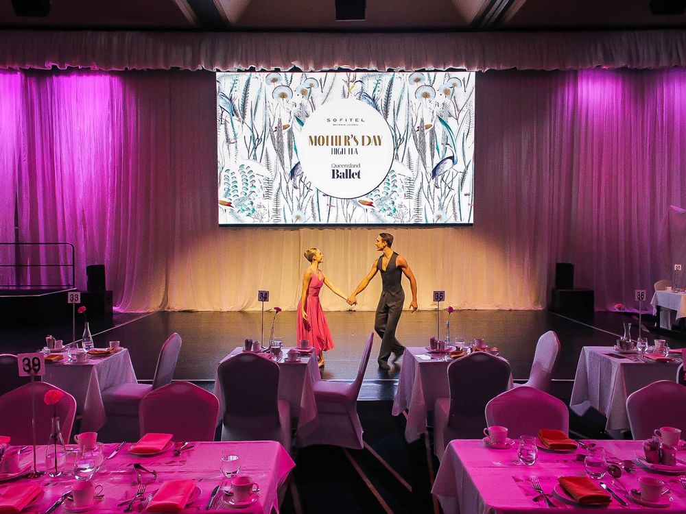 A couple holds hands and performs on a stage in Mother's Day High Tea event at Sofitel Brisbane Central