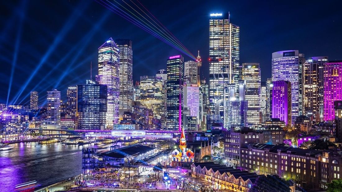 A city skyline at night with buildings and colorful lights for Vivid Sydney 2026.