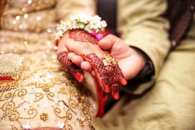 Bride and groom holding hands at The Saujana Hotel Kuala Lumpur, with henna, gold jewelry, and a richly decorated backdrop