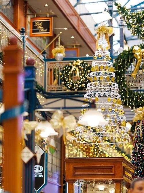 Festive shopping mall interior with illuminated Christmas tree, golden decorations, and holiday lights adorning multiple levels