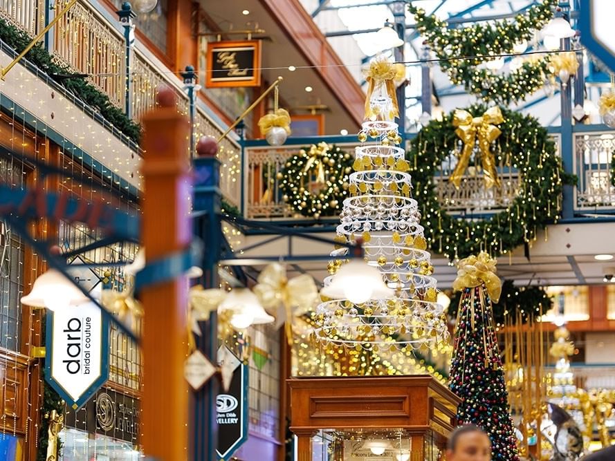 Festive shopping mall interior with illuminated Christmas tree, golden decorations, and holiday lights adorning multiple levels
