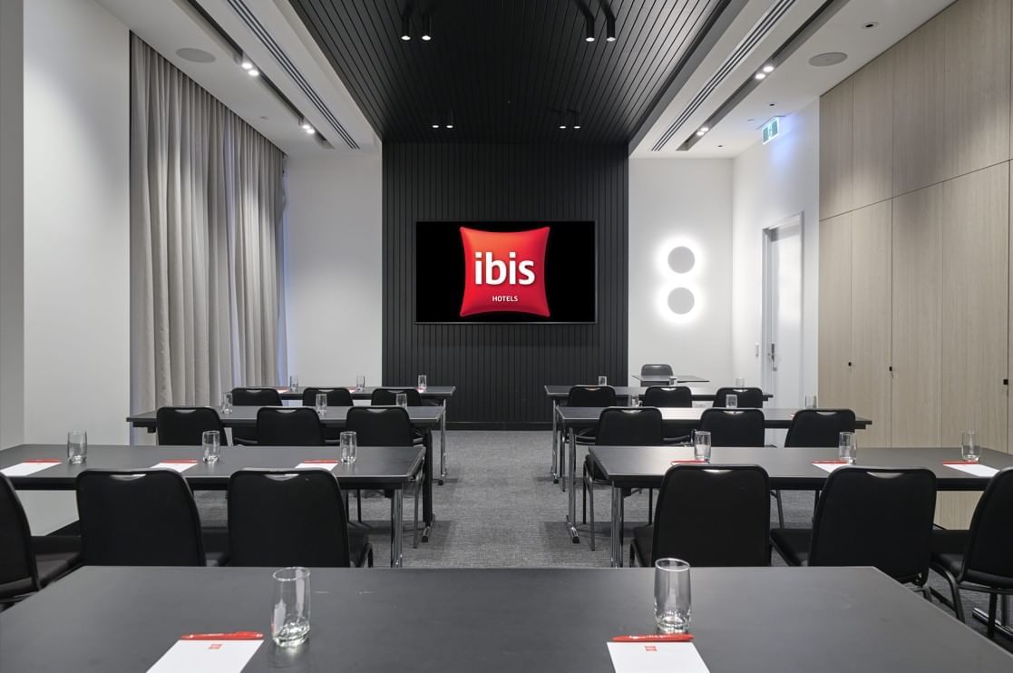 Classroom-style table set up facing the wall-mounted TV in The Junction at Ibis Adelaide