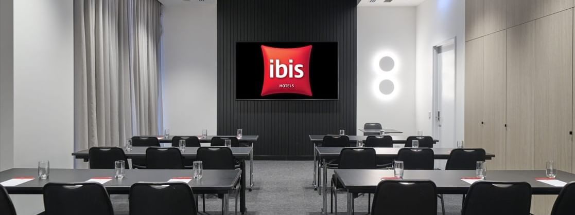 Classroom-style table set-up facing a large screen in The Junction at Ibis Adelaide