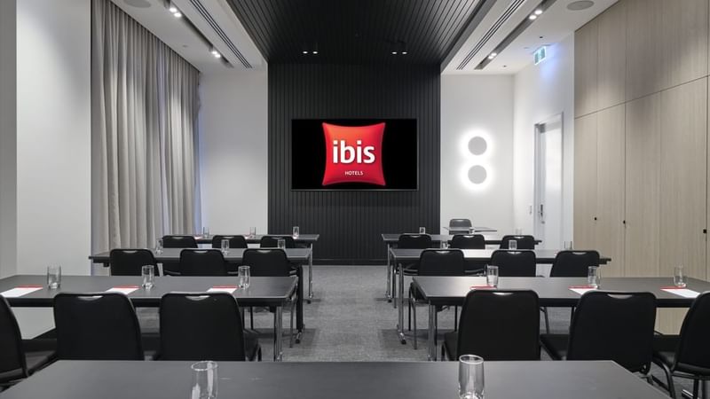 Classroom-style table set-up facing a large screen in The Junction at Ibis Adelaide