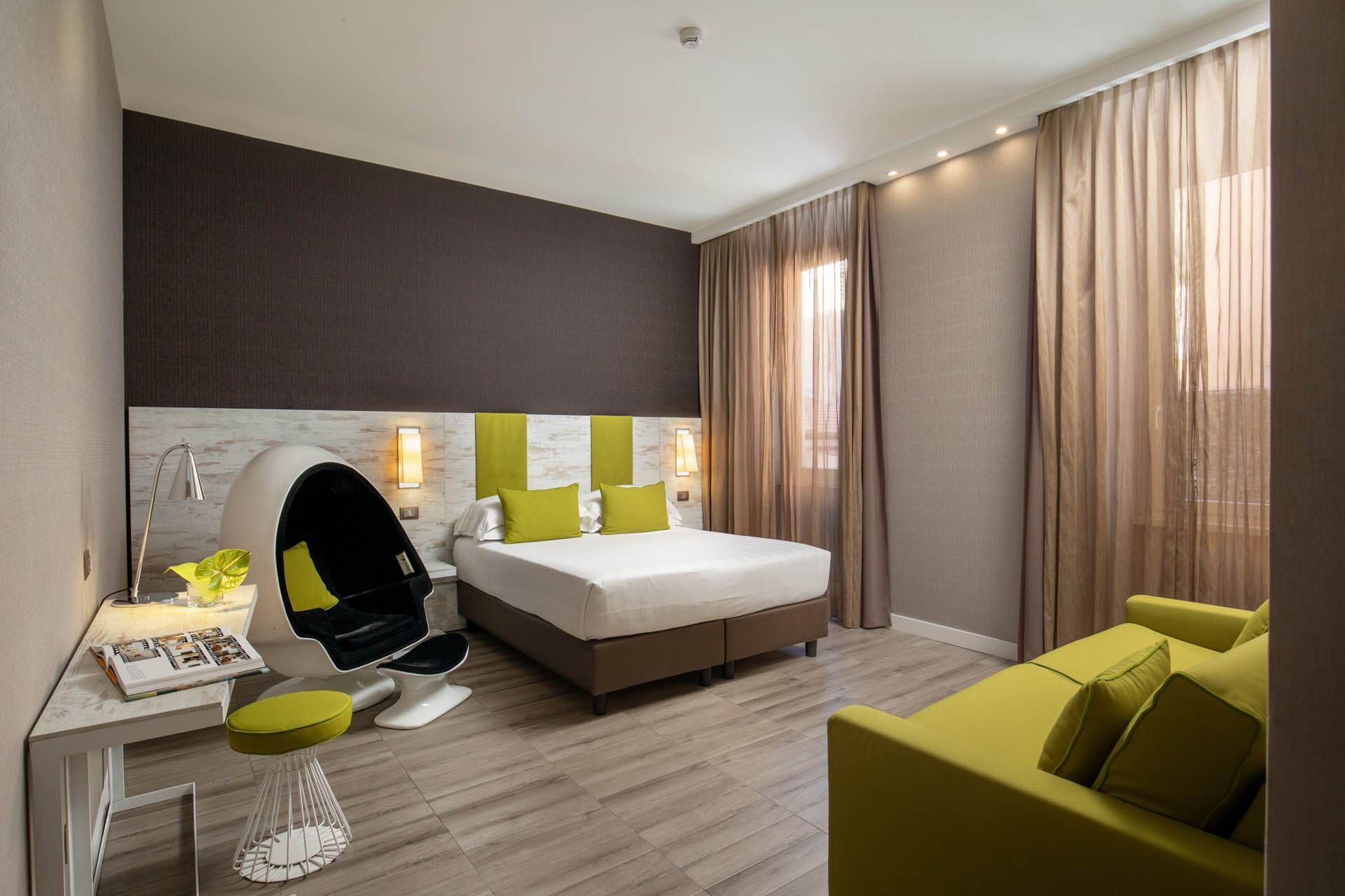 Modern room at The Guardian Hotel with a double bed, egg chair, green accent sofa, and plenty of natural light