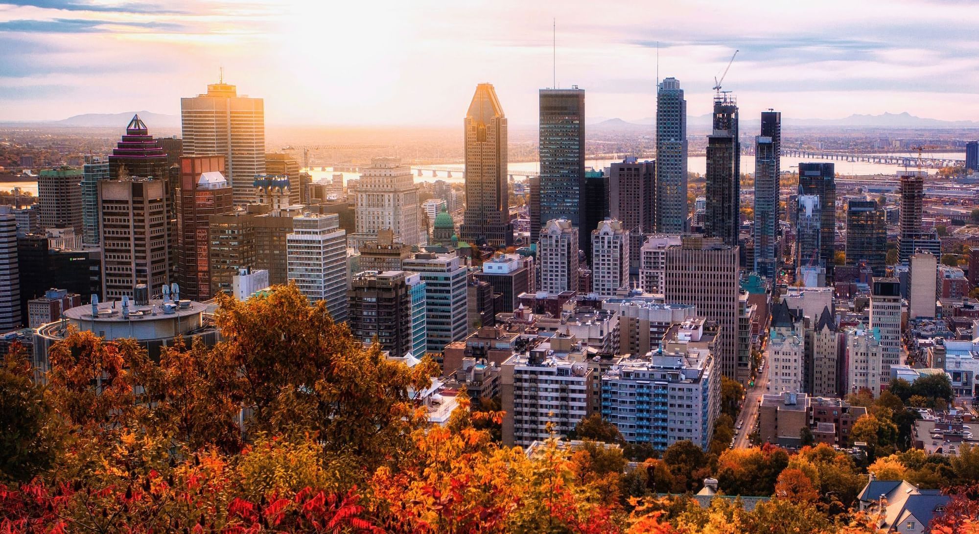 Sunset over a city skyline with autumn-colored trees in the foreground near Warwick Hotels and Resorts