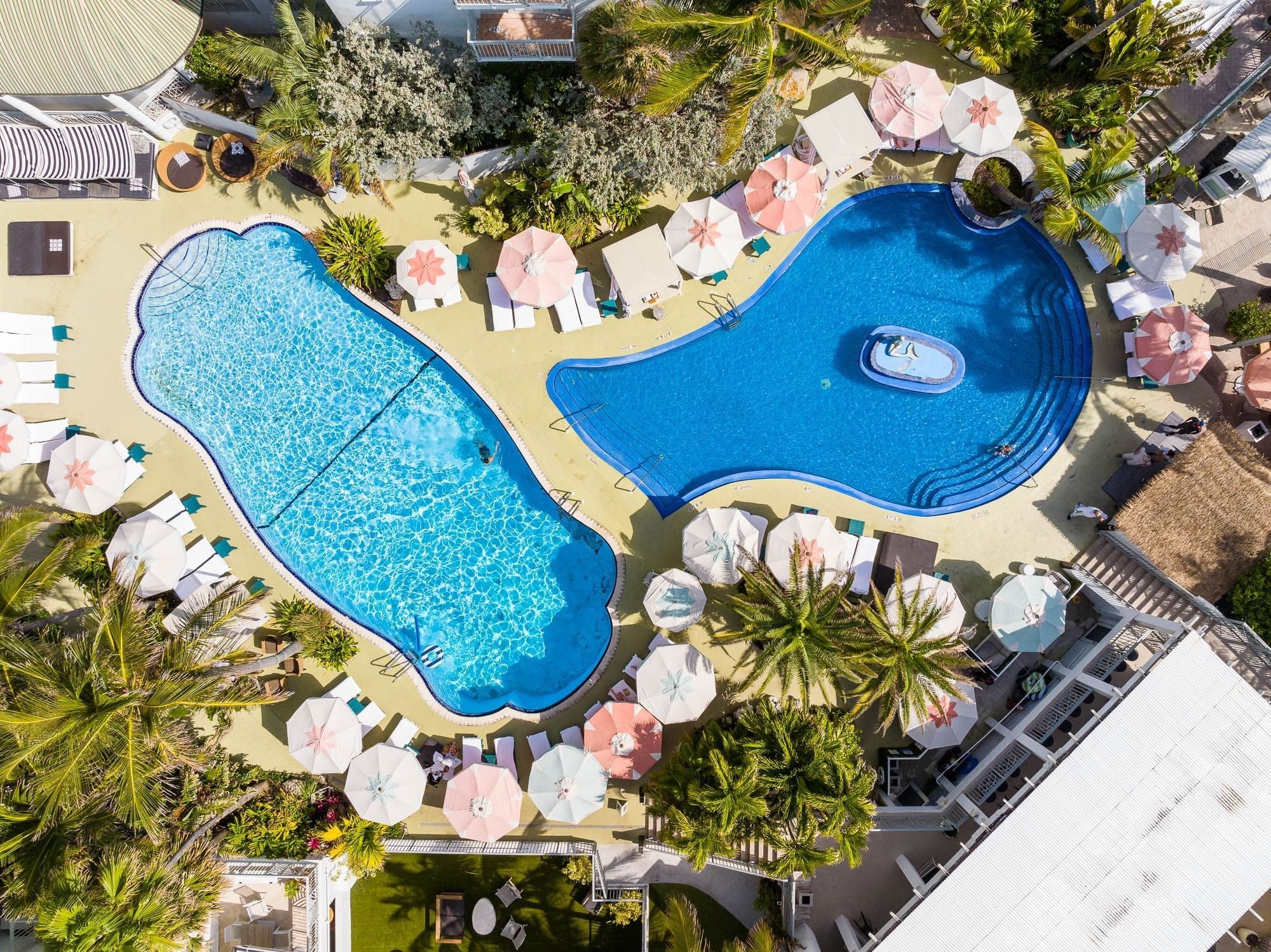 An aerial view of a hotel pool area with a large pool, lounge chairs, and umbrellas.