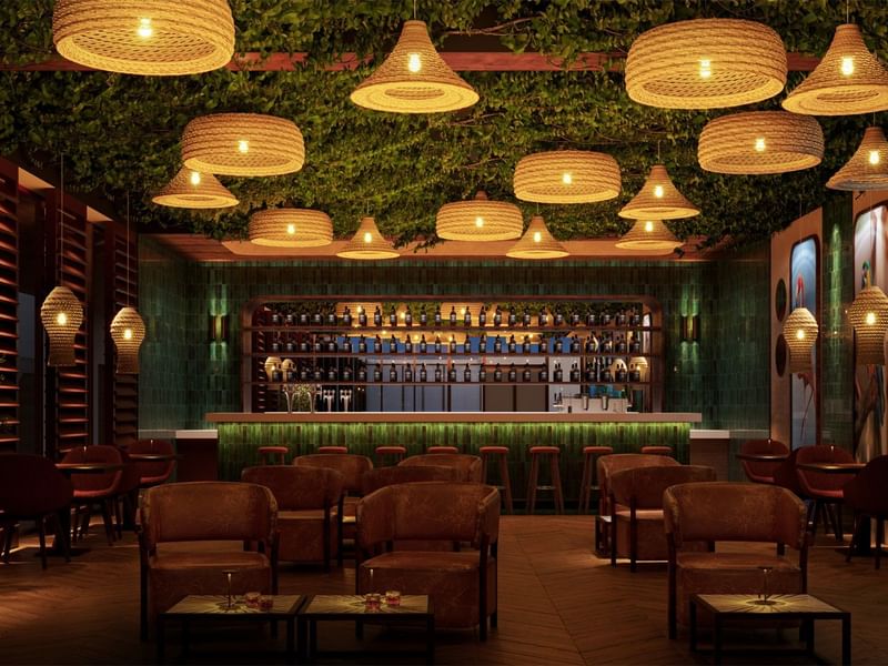 Lobby bar tenuemente iluminado en Fiesta Americana Funeeq con lámparas tejidas, sillones marrones y paredes verdes