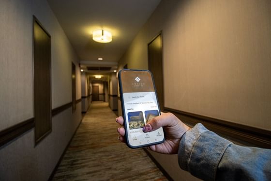 Person holding a smartphone in a hallway by doors under a glowing ceiling light at Hotel Mirra