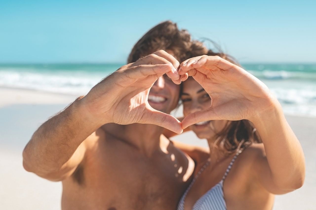 Pareja feliz formando un corazón con las manos en la playa tropical soleada cerca de Fiesta Americana Funeeq