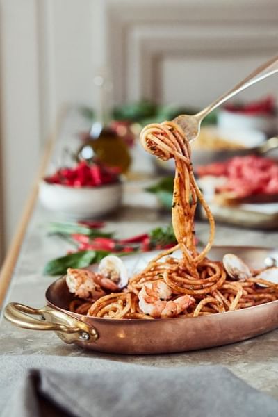 Fork twirling shrimp spaghetti in a copper pan surrounded by fresh ingredients in Opera Restaurant at Park Hyatt Saigon