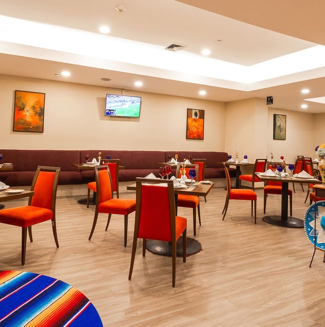 Modern dining area featuring red seating with colorful decor and sports TV screens at Camino Real Aeropuerto Mexico