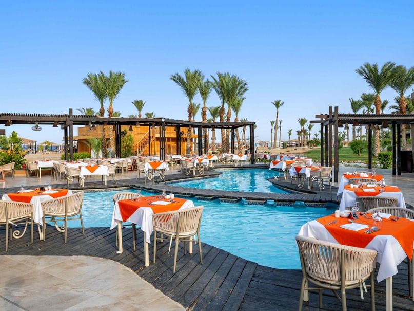 Outdoor dining area with tables and chairs by the pool at Cardamom A La Carte, Pickalbatros Palace Hotel, Red Sea Governorate.