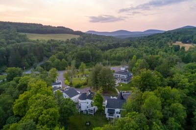 Aerial view of The Roxbury surrounded by greenery featuring unique houses and a mountain backdrop
