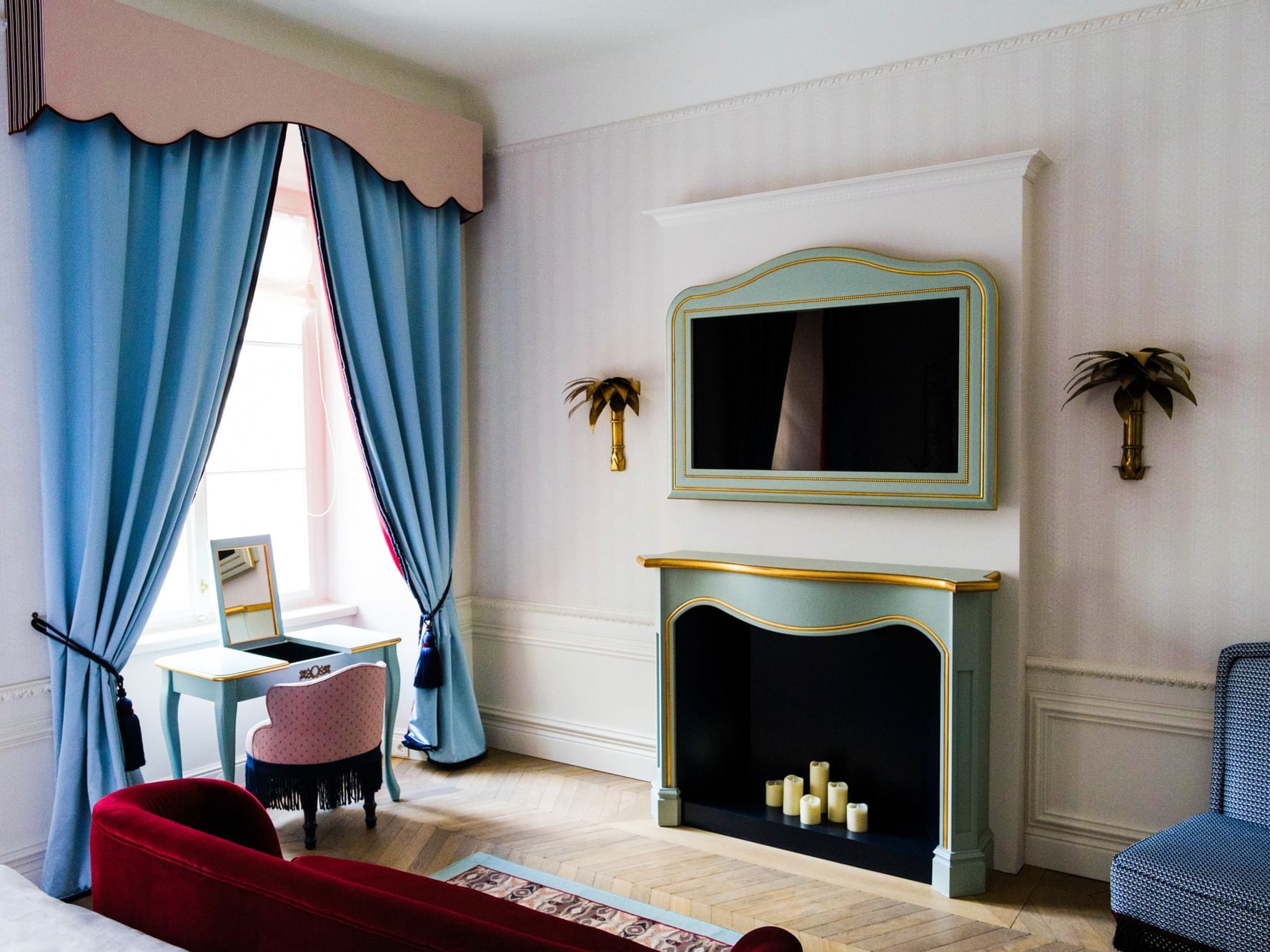 Elegant room with blue curtains, fireplace, framed TV, small desk with mirror, and two chairs near a window.