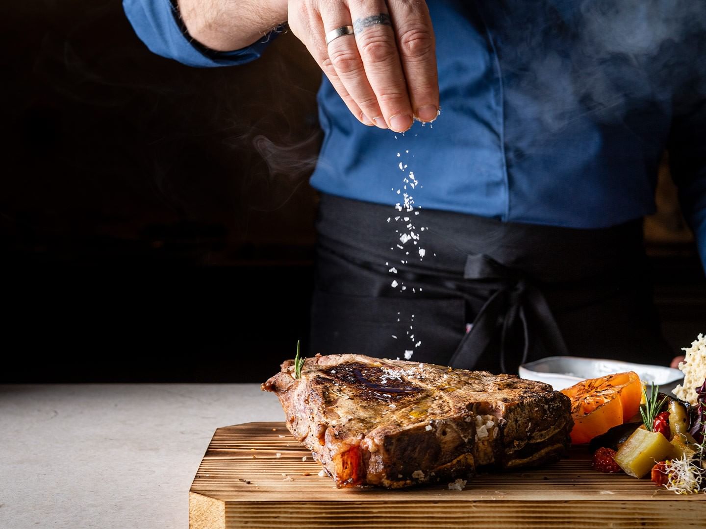 Chef seasoning steak on a wooden board at 12 Hoefe – La cucina dei 12 masi, Falkensteiner Family Resort Lido, Ehrenburg.