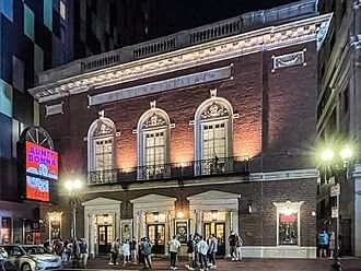 Crowded entrance of a theater at night with lit signs and people waiting in line.