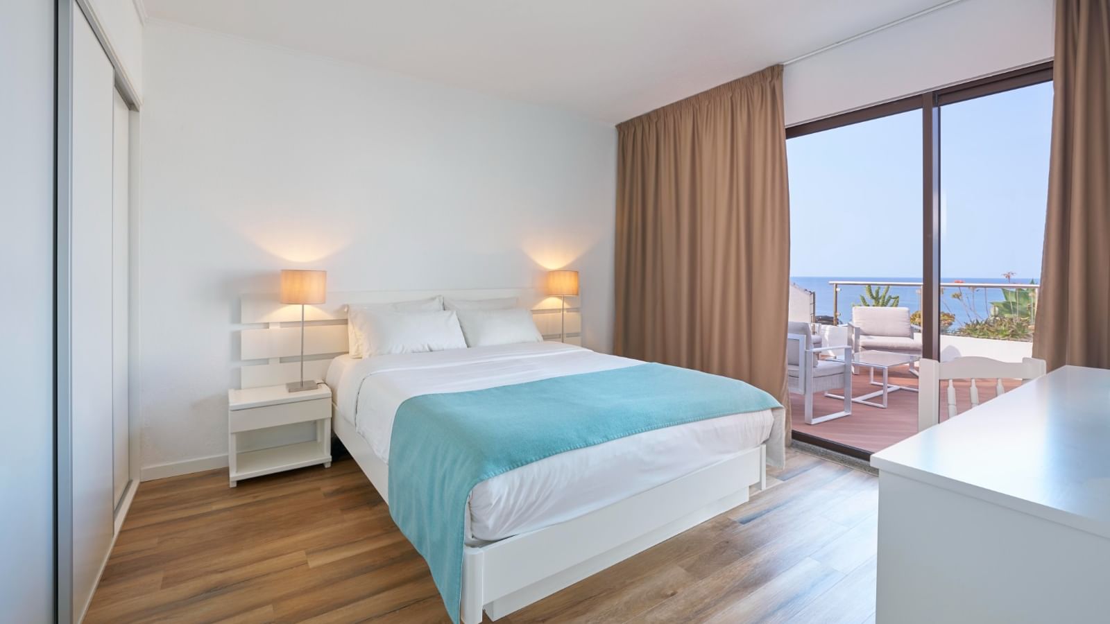 Nightstands by the cozy bed in the Suite with wooden flooring and a balcony seating area at Bensaude Hotels