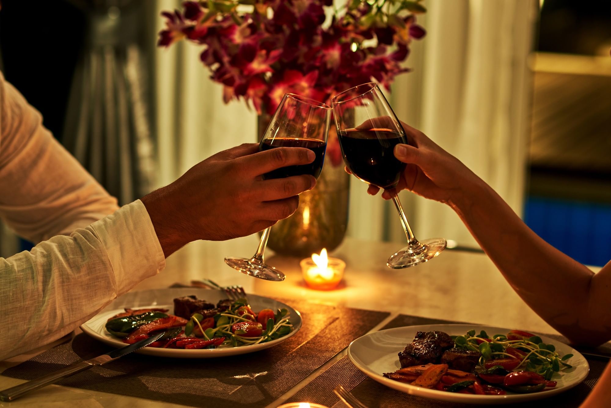 Two people toasting with wine glasses over dinner plates with meat and vegetables at Warwick Allerton Chicago
