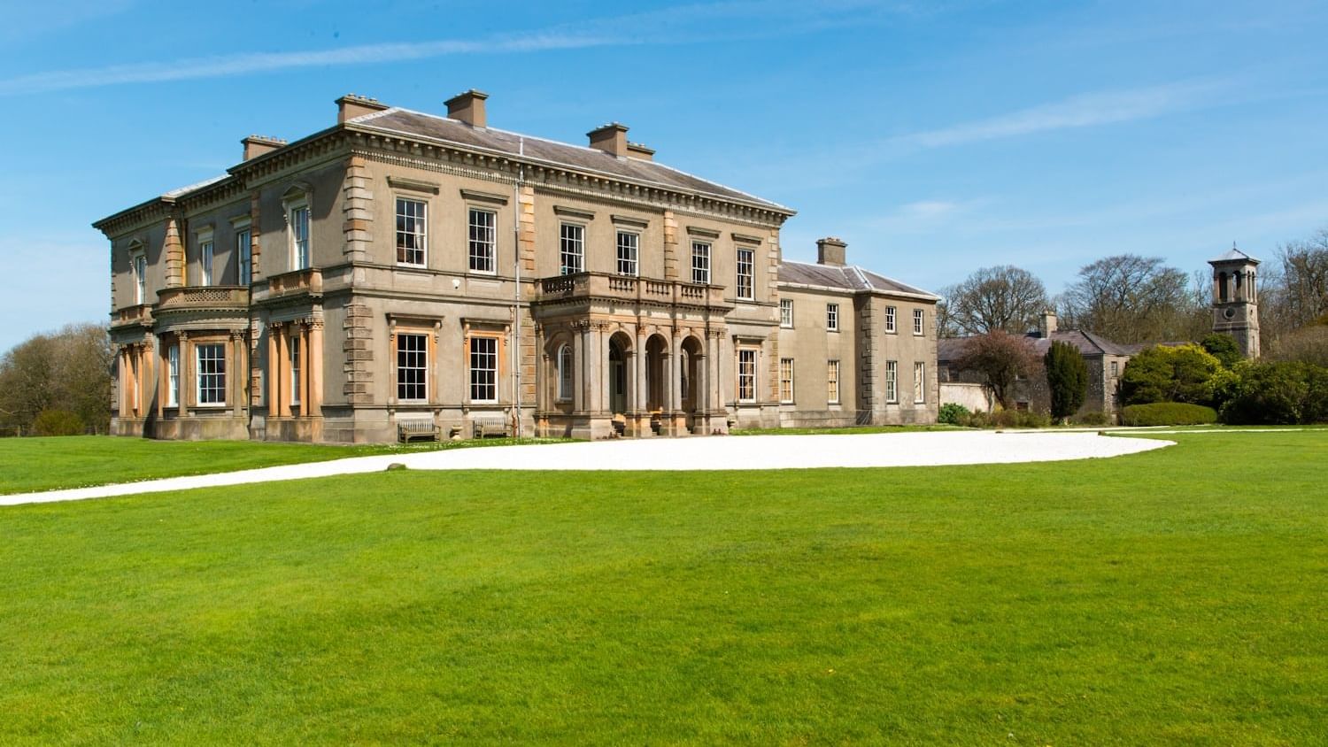 A grand historic manor house with a large green lawn, an elegant sight near Dunluce Lodge