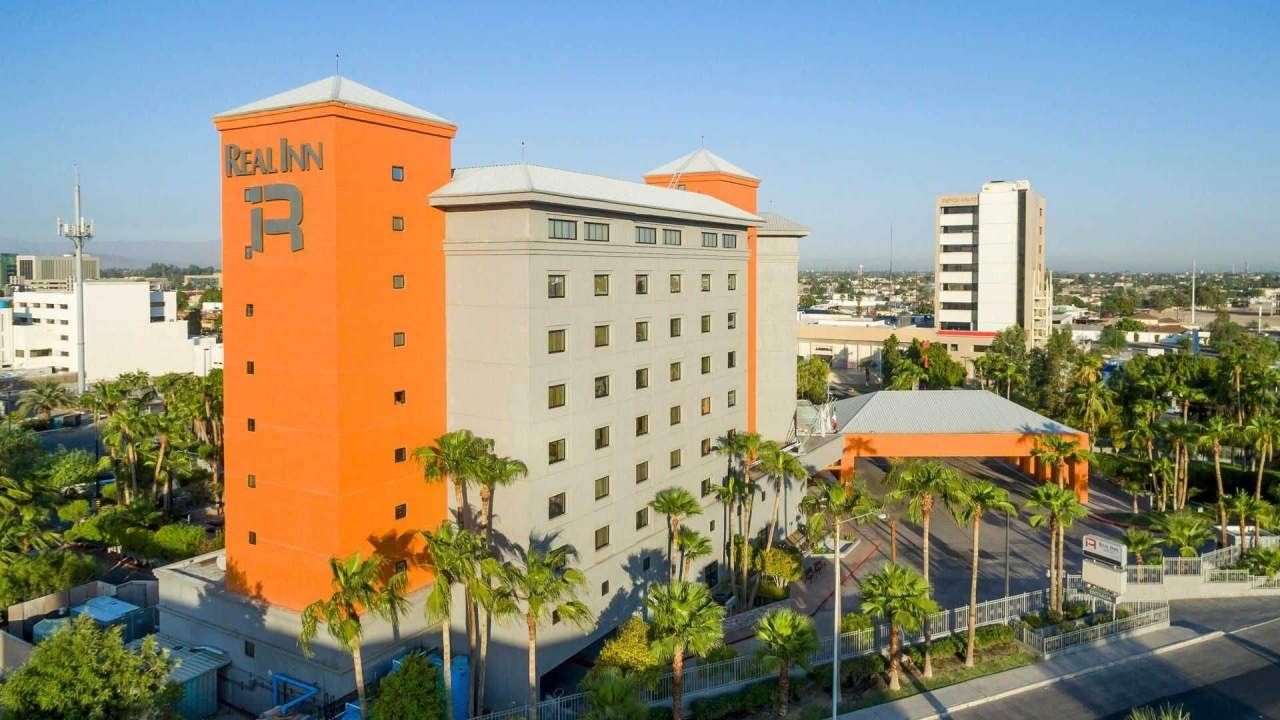 Exterior of the Real Inn hotel with a bright orange tower and palm trees near Camino Real Pedregal Mexico
