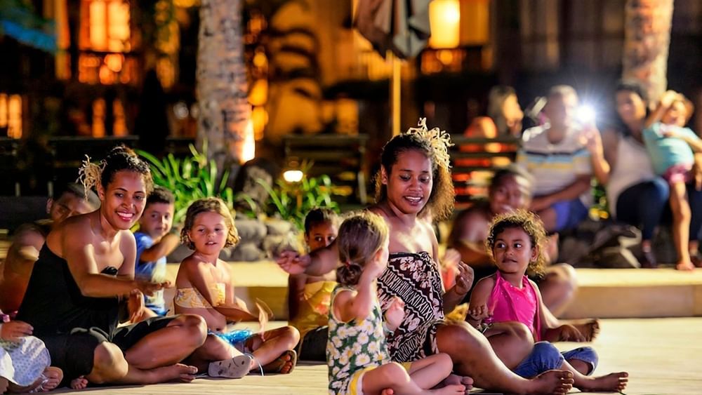 Performers in traditional dress by children under warm lights in a courtyard at The Naviti Resort - Fiji