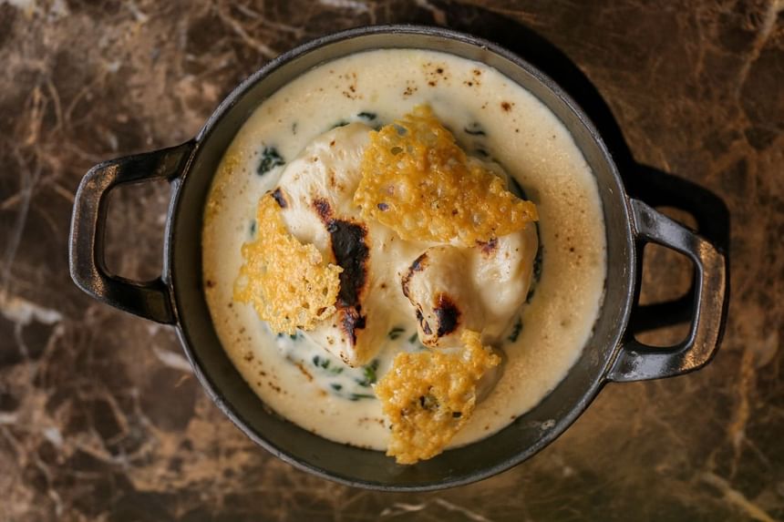 Creamy spinach dish topped with crispy cheese shards, served in a black skillet on a marble backdrop at Park Hyatt Saigon
