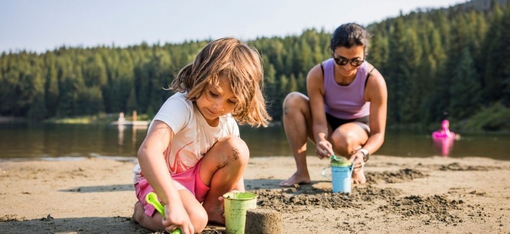 Child playing on a sandy Whistler lake beach with a parent nearby