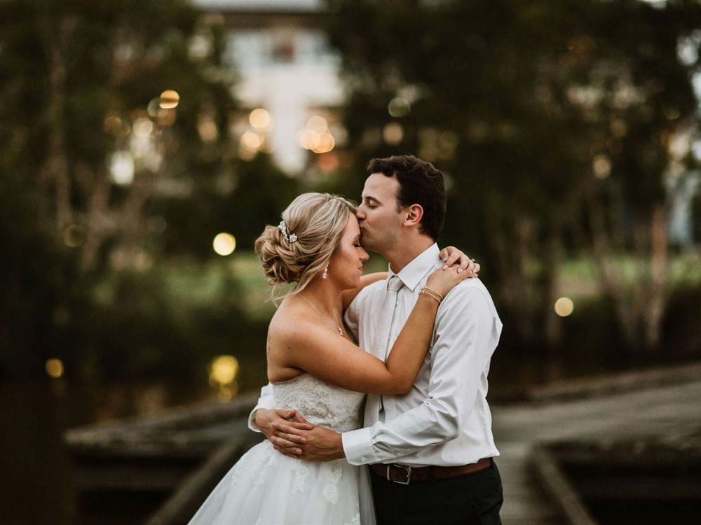 Bride and groom in an outdoor setting with trees and blurred lights in the background.