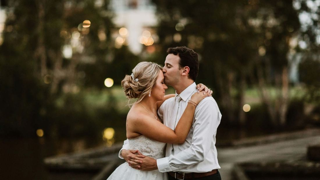Bride and groom in an outdoor setting with trees and blurred lights in the background.