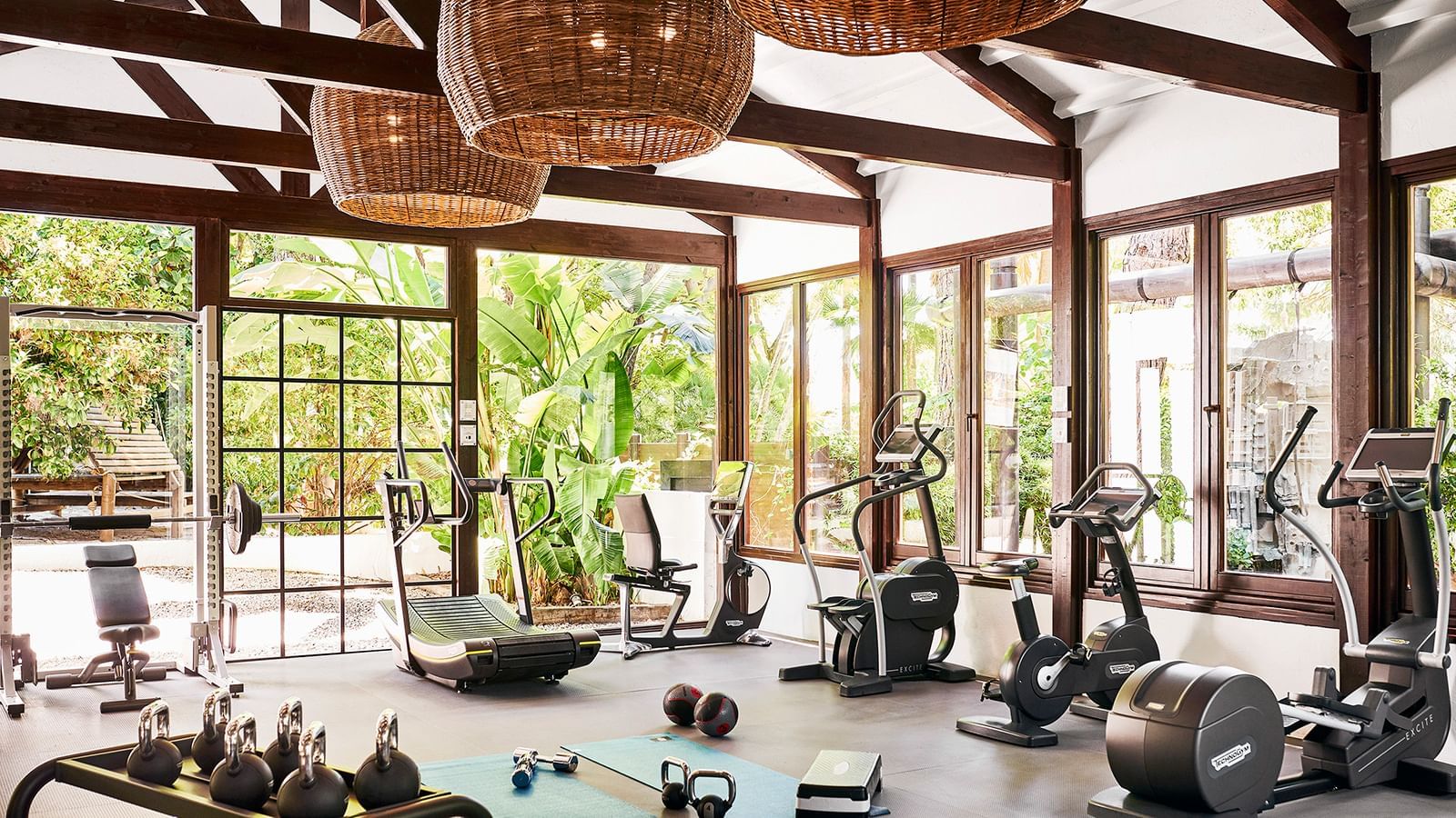 Gym with cardio machines placed by floor-to-ceiling windows under woven light fixtures at the Marbella Club